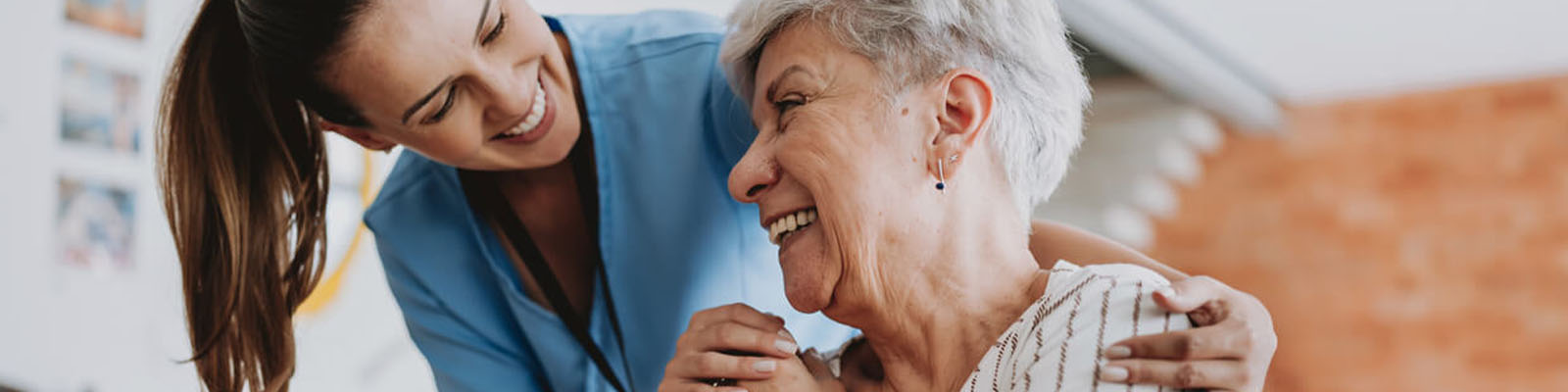 A female senior living nursing assistant leaning down to smile at a female senior resident sitting in a wheelchair