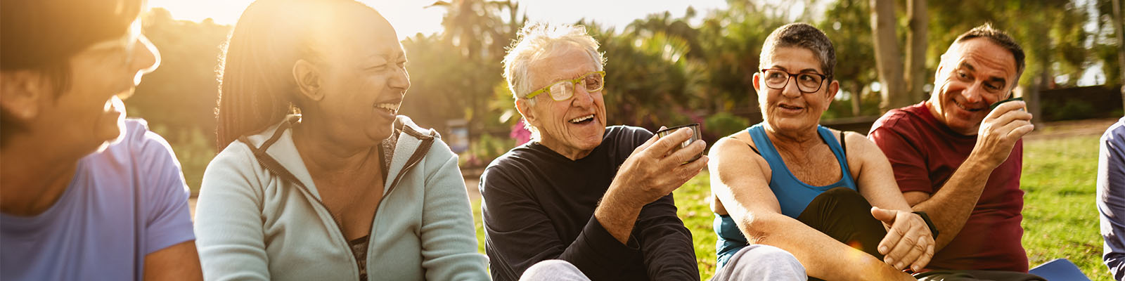 A group of male and female senior living residents sitting outside talking and laughing in the grass